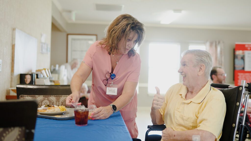 a nurse assists a woman at dinner in a long term care center