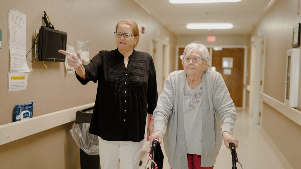 A woman walking down a hallway with a resident at a skilled nursing facility that offers long-term care services