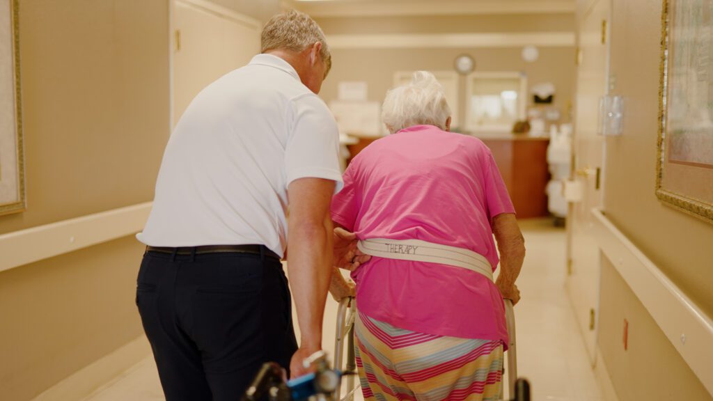 A man and resident walk down a hallway at a skilled nursing facility