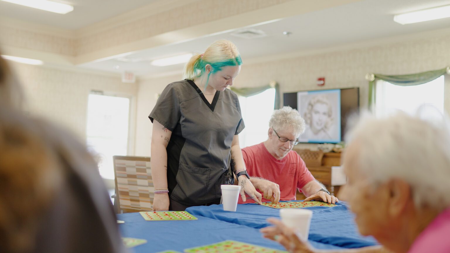 A nurse assists a man in a game of bingo at a skilled nursing facility
