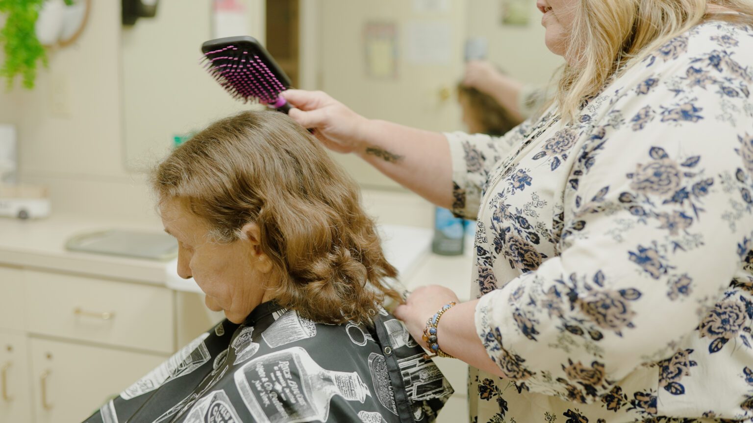 A stylist brushes a resident's hair at a salon at a skilled nursing facility